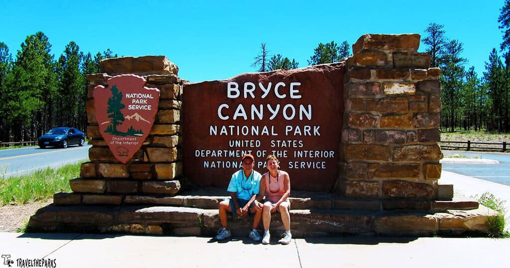 Stone sign for Bryce Canyon National Park with two people sitting in front of it.
