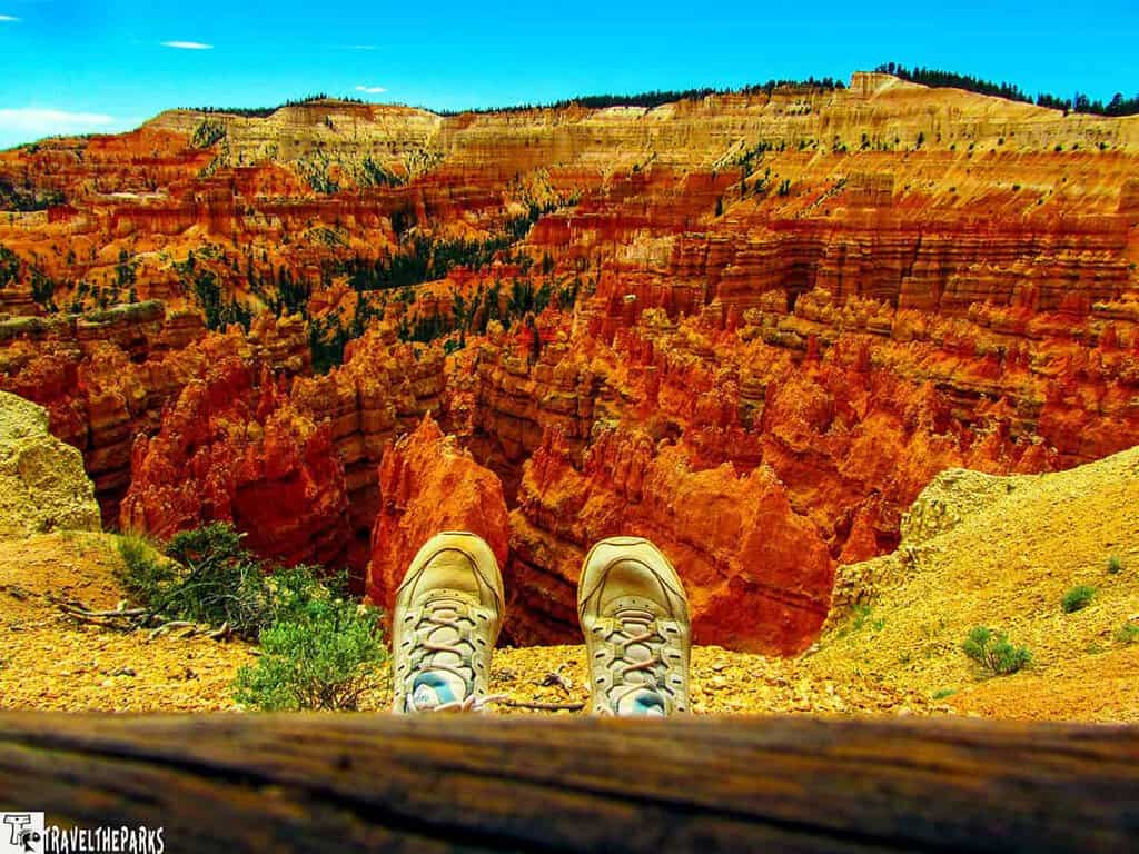 A view of Bryce Canyon with hiking shoes in the foreground and vibrant orange-red rock formations in the background.
