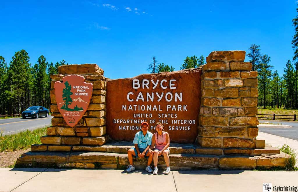 Stone sign for Bryce Canyon National Park with two people sitting in front of it.