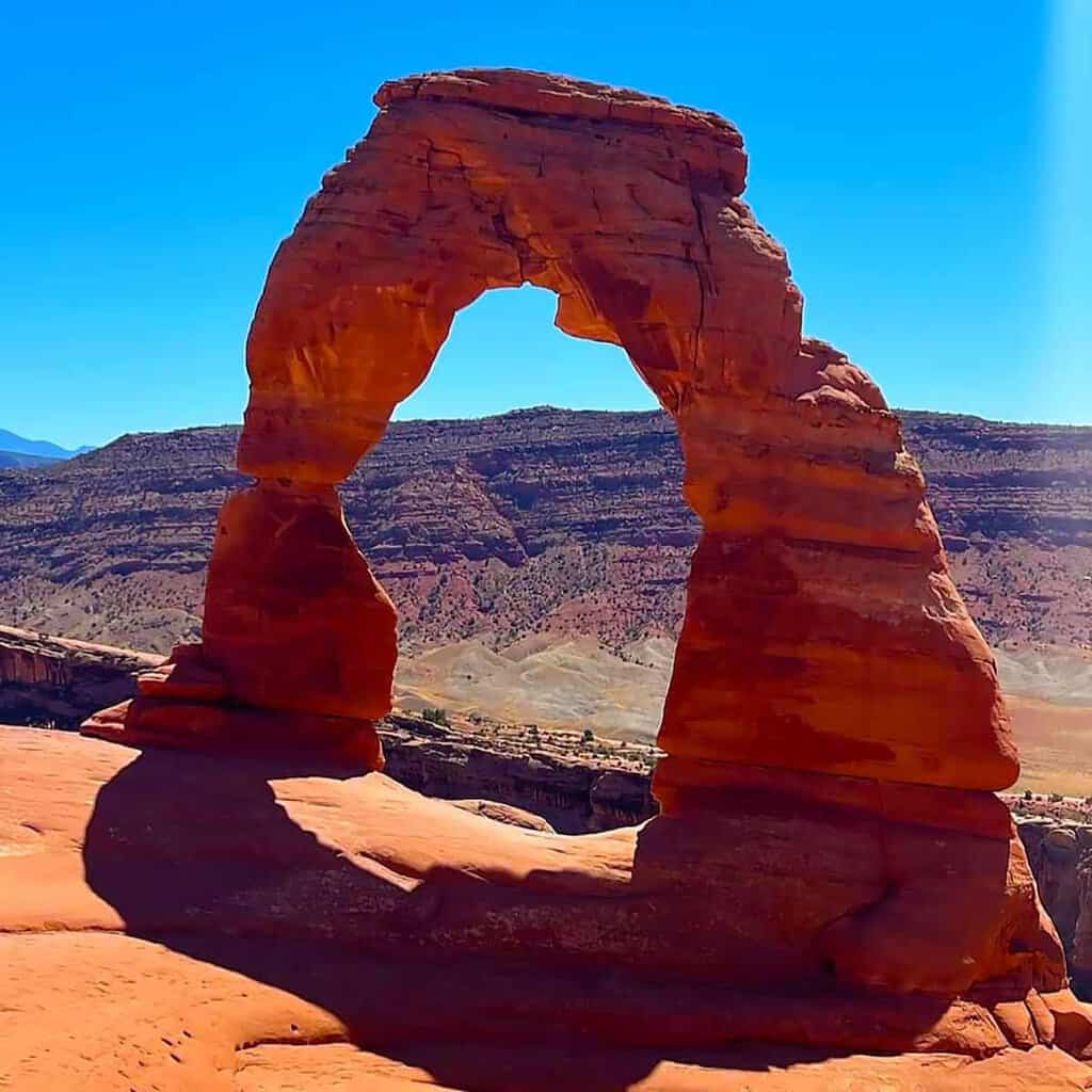 Delicate Arch in Arches National Park with distant mountains and a partly cloudy sky.