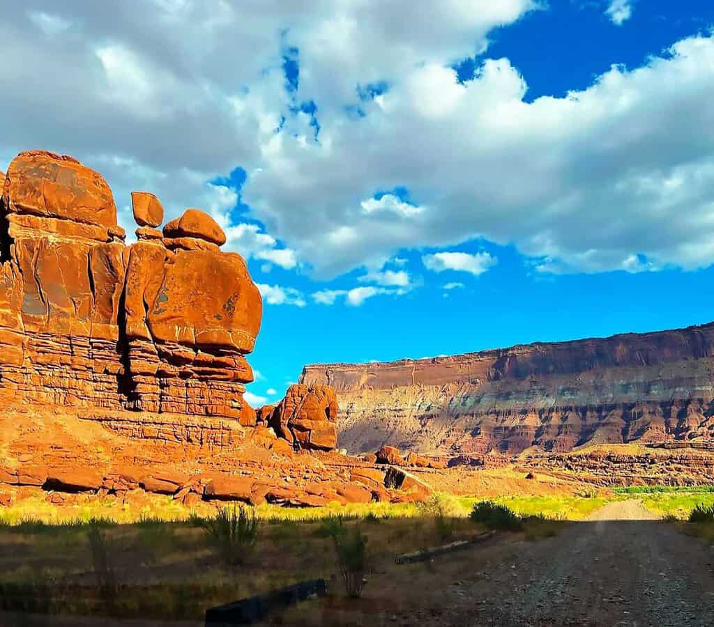 Desert landscape with large rock formations and a distant mesa under a blue sky with clouds.