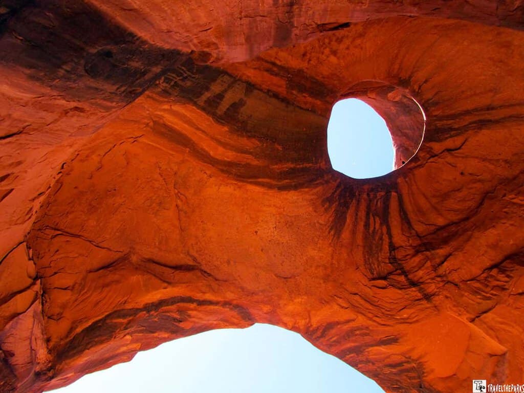 Eagle-Head-at-Big-Hogan-A view looking up at a hole in a red rock formation, with blue sky visible through the opening.