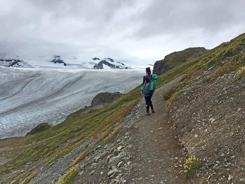 Hiker on a path beside Harding Icefield under overcast skies.