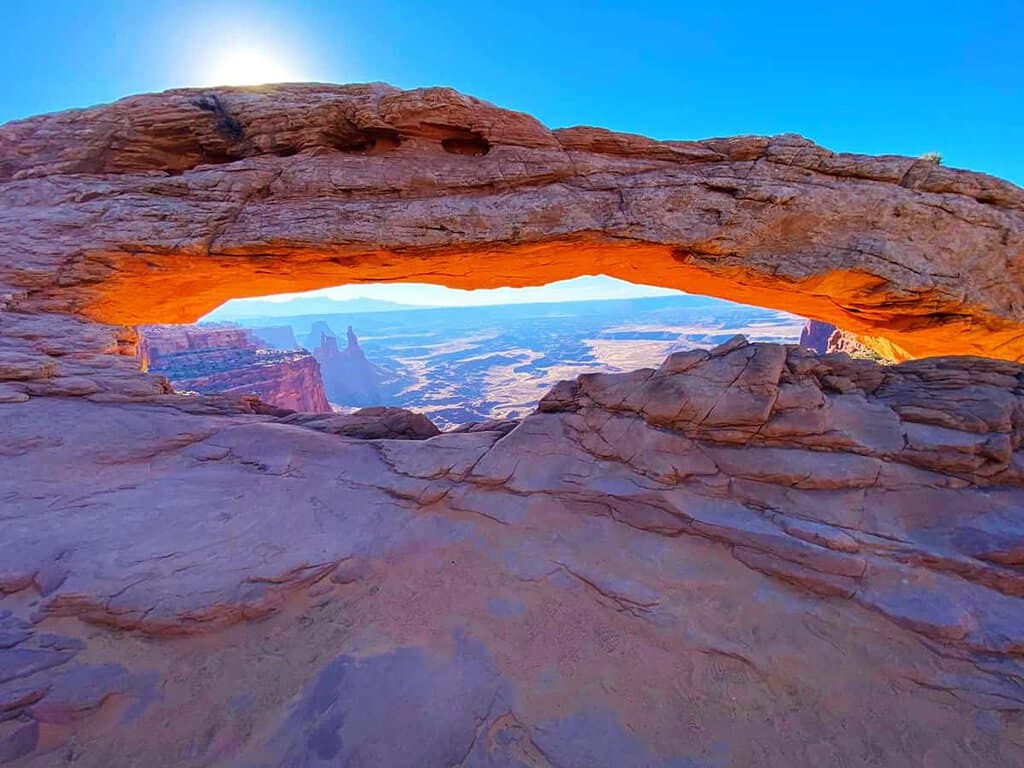 A natural arch with a sunlit landscape in the background, viewed from beneath the arch