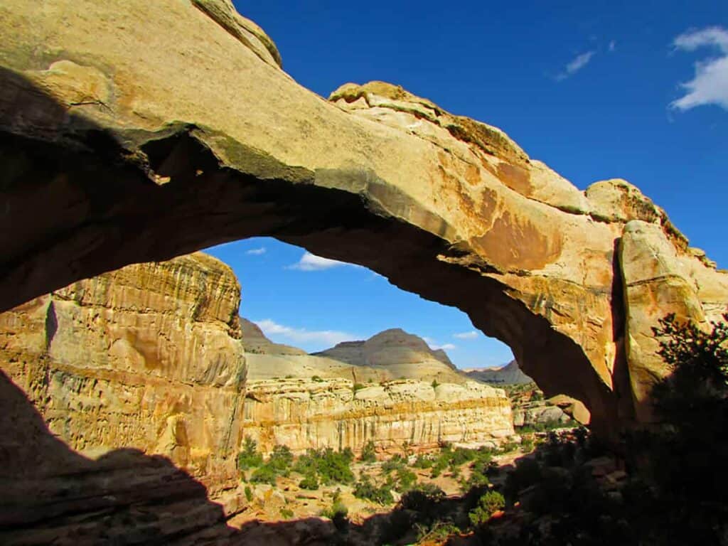 Hiking to a natural rock arch in Capitol Reef National Park with distant rock formations and clear blue sky.