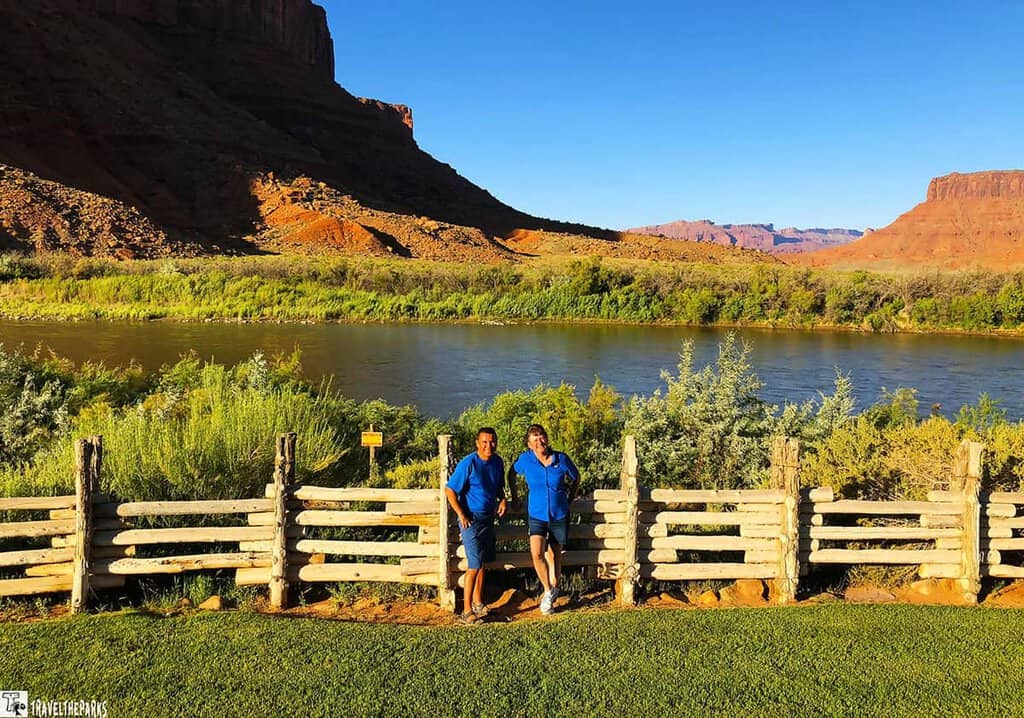 Two people stand by a wooden fence with a mountain range in the background, near Red Cliffs Lodge.