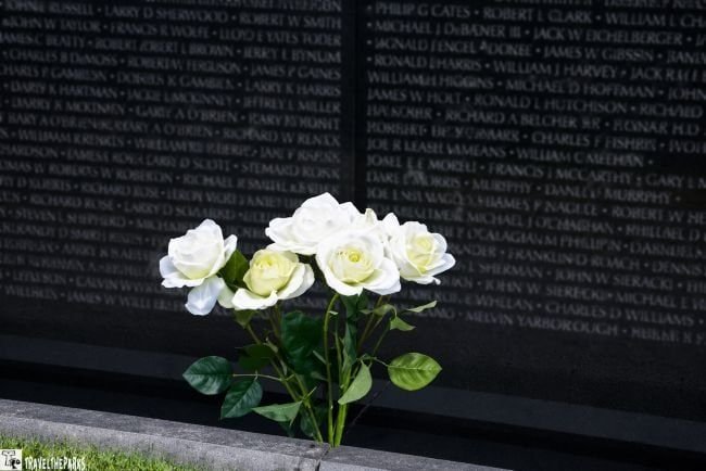 Names on the Vietnanm Wall memorial wall with white roses at the base.