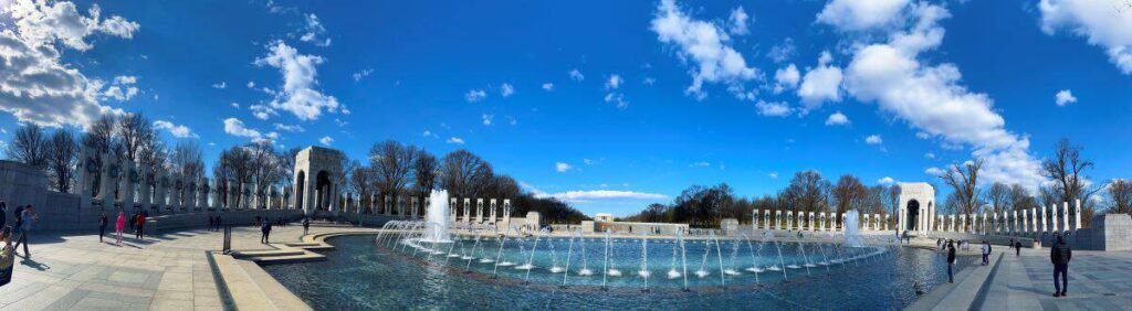 Panoramic view of the National World War II Memorial with a central fountain, columns, and clear blue sky.