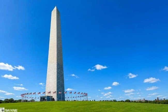 The Washington Monument with American flags at its base against a blue sky.