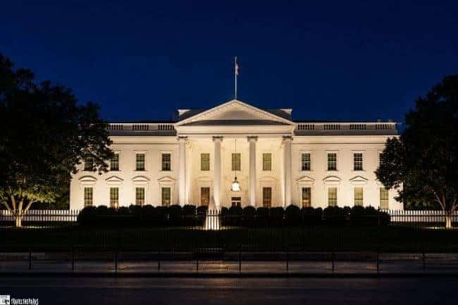 The White House illuminated at night with a flag on the roof and trees on either side.