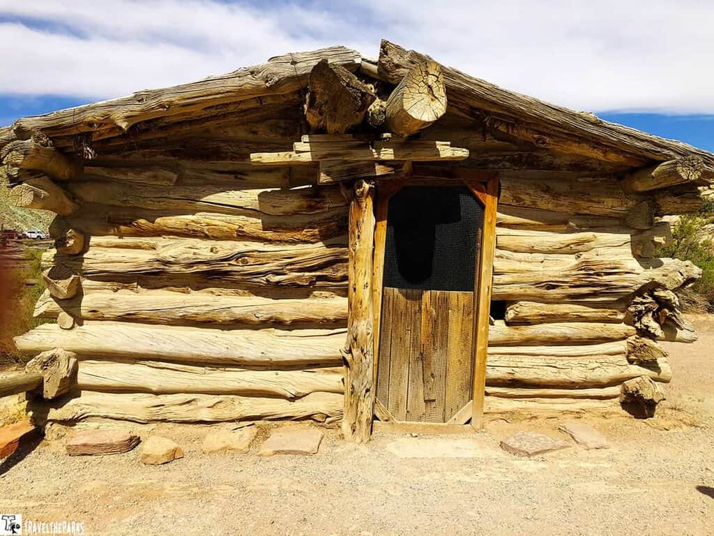Wolfe Creek Cabin-A rustic log cabin with a wooden door and mesh window in an arid landscape.