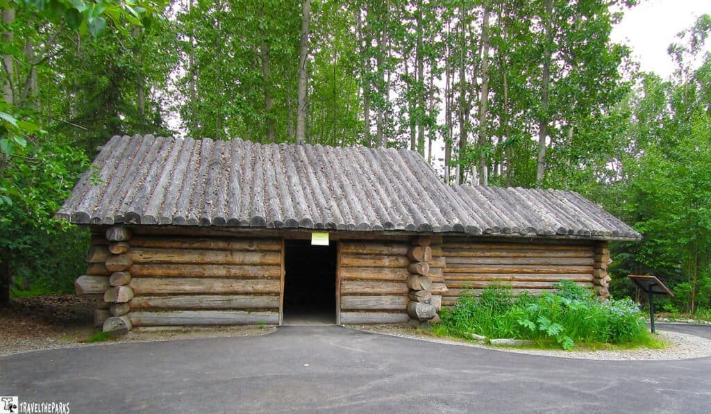 Athabaskan Village Lodge Traditional log cabin with a wooden roof in a forested area. At the Alaska Native Heritage Center