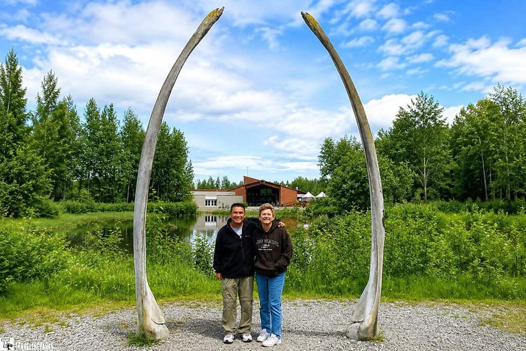 Two people stand beneath a whale bone archway Lake Tiulana at the Alaska Native Heritage Center.