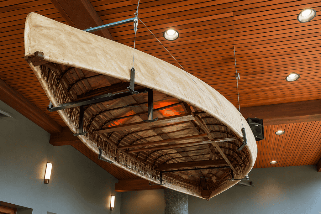 Weathered wooden canoe hangs upside down from cables beneath a warm slatted ceiling in a rustic dining space, creating a nautical focal point.