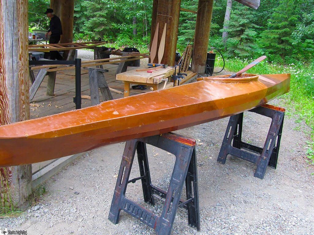 Wooden kayak on sawhorses in an outdoor workshop surrounded by trees at the Alaska Native Cultural Center Village.