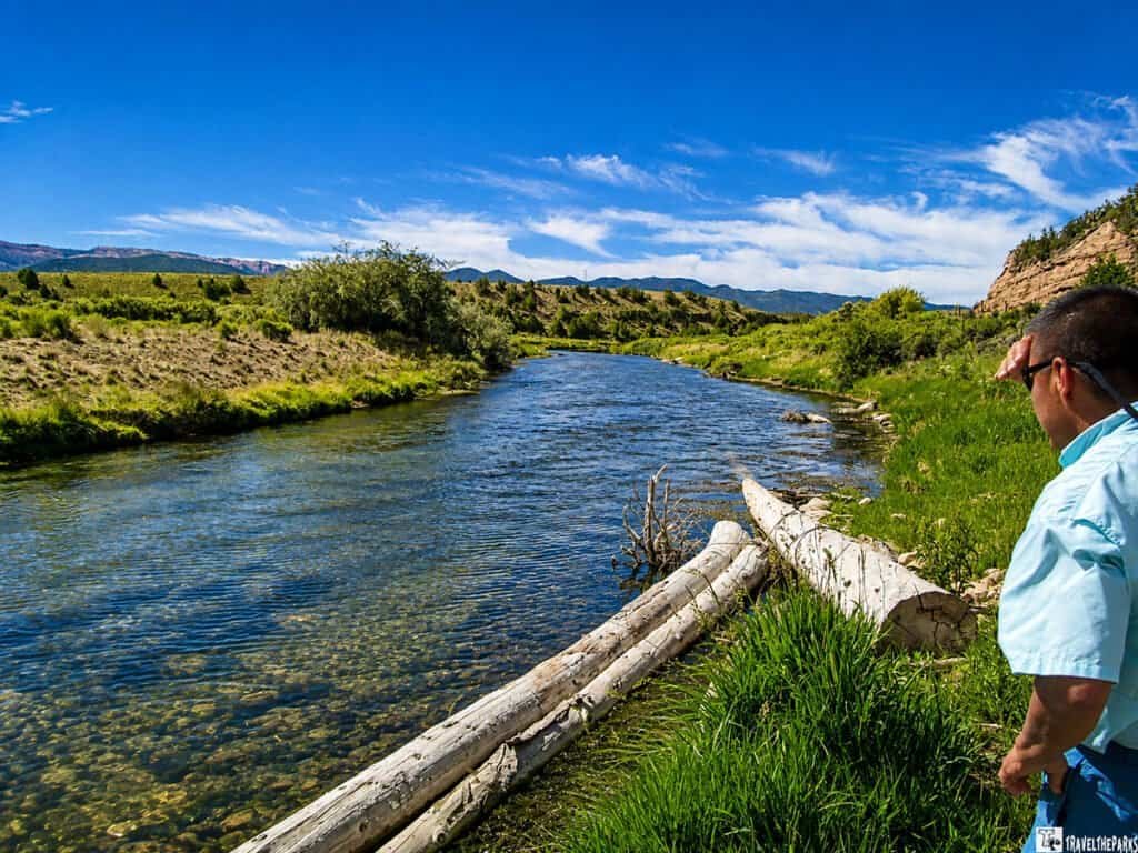 A calm Sevier river flowing through a grassy landscape under a blue sky with clouds.