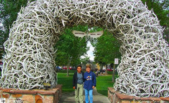 Jackson Town Center Park an arch made of pale antlers with a stone base, located in a park with trees and two people in front.