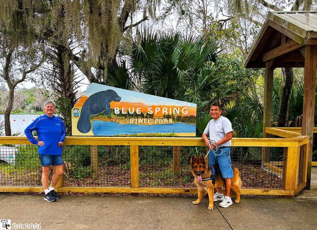 Two people and a dog in front of a Blue Spring State Park sign.