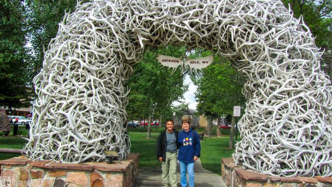 Archway made of interwoven antlers in a park in Jackson WY, with two people standing underneath.