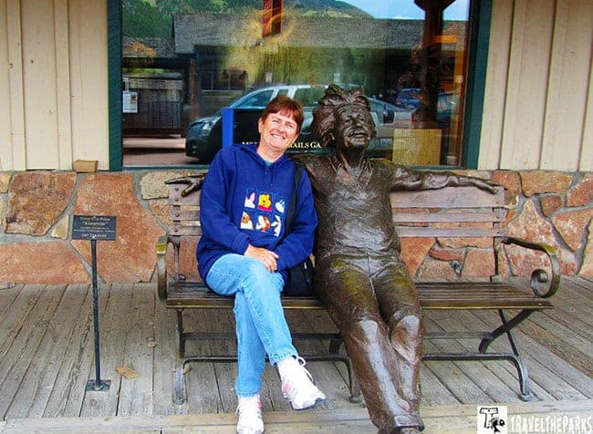 A woman seated on a bench next to a bronze statue of Einstien in front of a shop window in Jackson Wyoming Town Square.