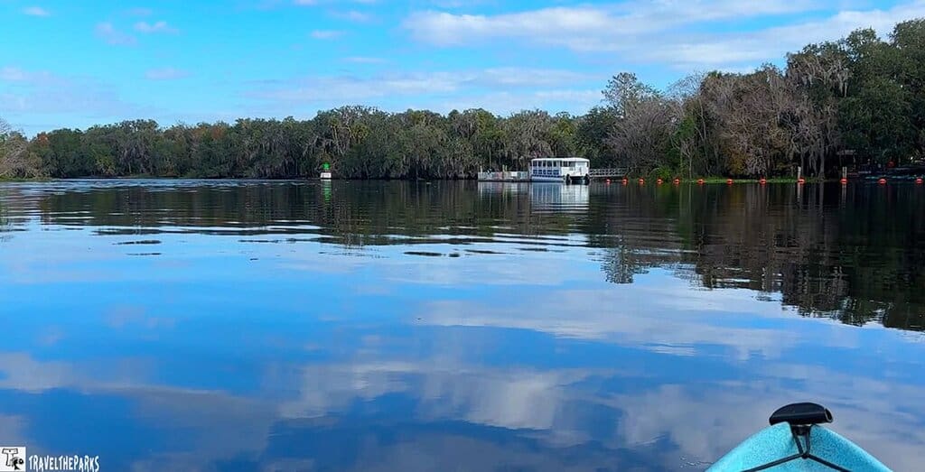 A calm lake at Blue Springs State Park with a boat and trees in the distance, viewed from a kayak.