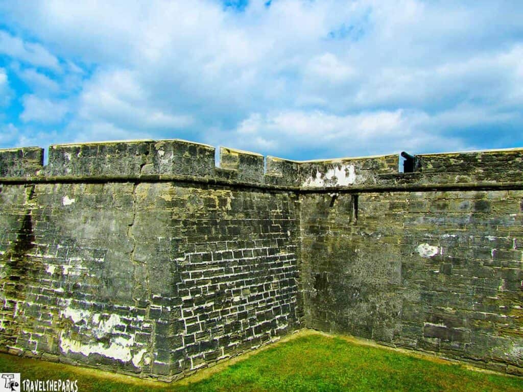 Stone walls of Castillo de San Marcos with parapet and cannon under a partly cloudy sky.

