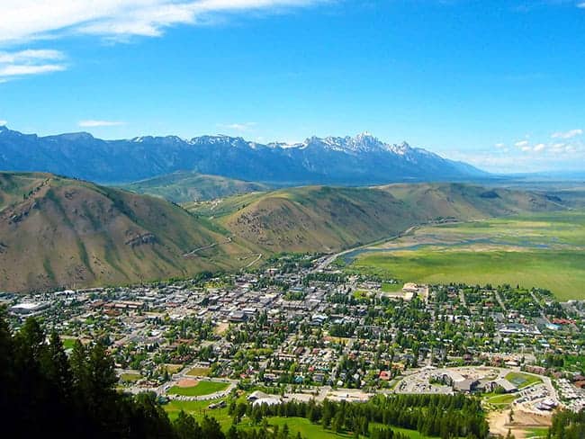 Aerial view of the town of Jackson, WY, in a valley surrounded by green hills and distant snow-capped mountains.