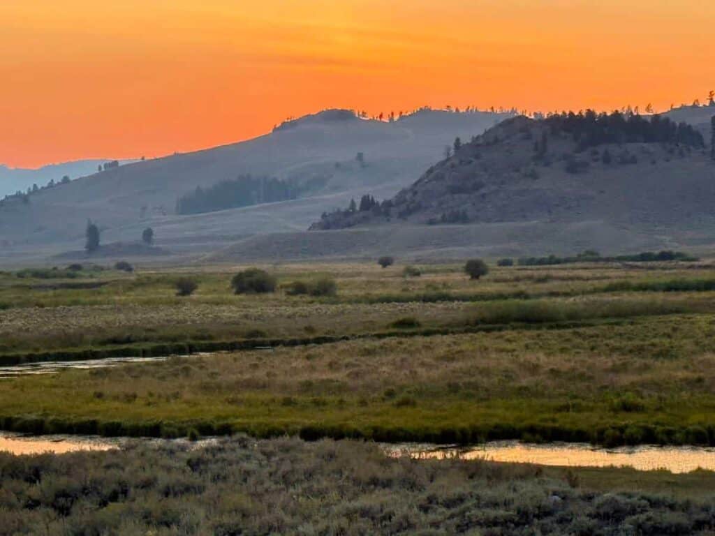 Sunset over grassy plains with rolling hills and a meandering river.