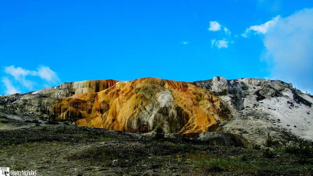 Colorful mineral terraces against a blue sky with clouds.

