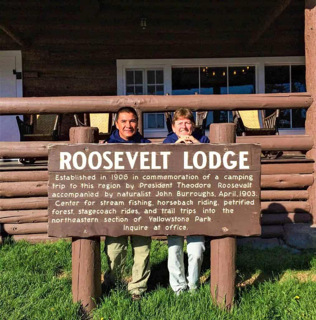 A woman poses in front of a sign that reads "Mammoth Springs," with a scenic background behind her at Yellowstone National Park.