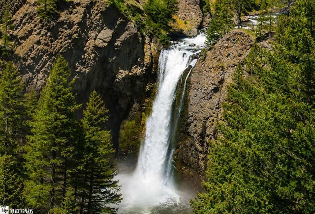 Tower waterfall flows down a rocky cliff, surrounded by evergreen trees.
