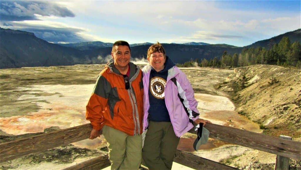 Two people on a deck overlooking Mammoth Hot Springs with mountains in the background.