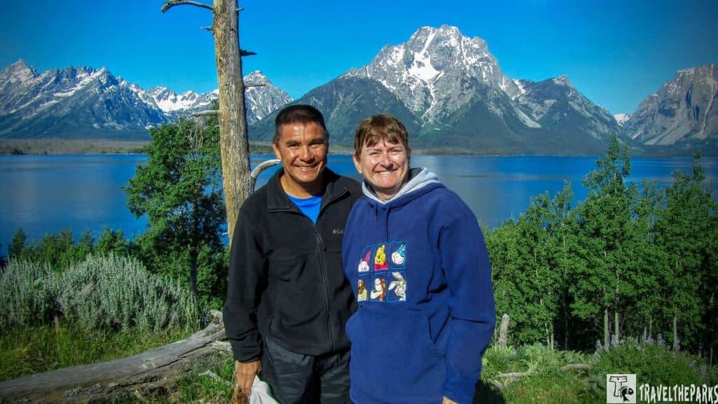 Elk Island Breakfast Cruise: Two people smiling in front of a lake and mountain landscape.