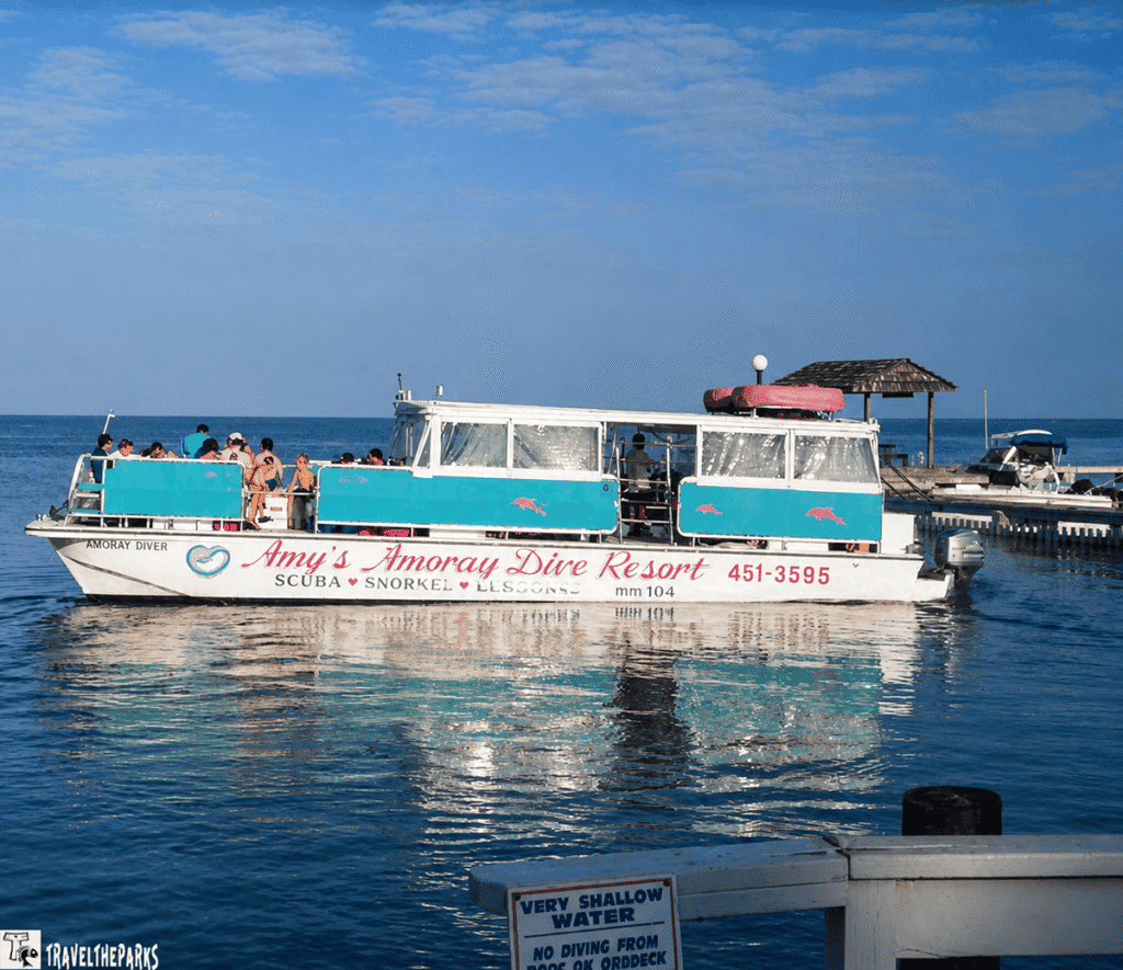 A boat named "Amoray Diver" on calm water with people aboard, under a blue sky.