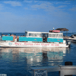 A boat named "Amoray Diver" on calm water with people aboard, under a blue sky.