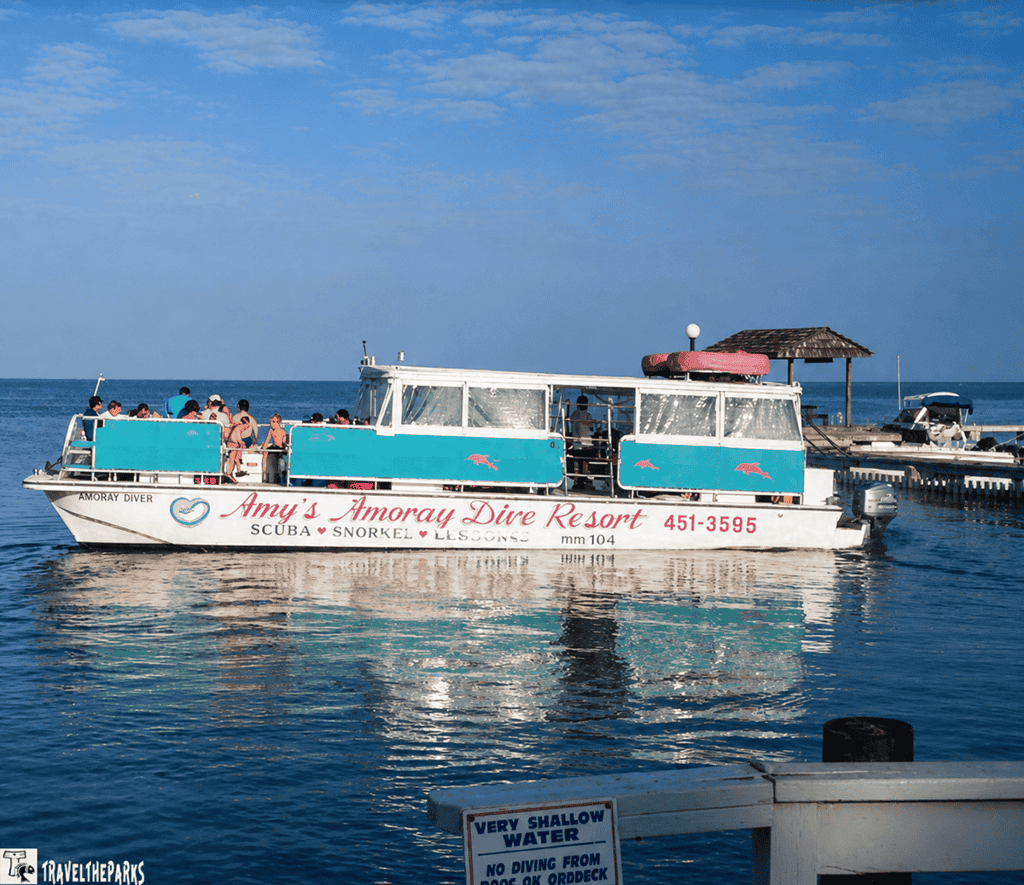 A boat named "Amoray Diver" on calm water with people aboard, under a blue sky.