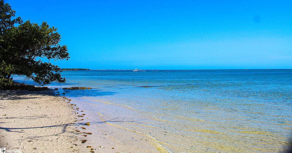 A tranquil beach with clear blue skies, gentle waves, and a distant boat.