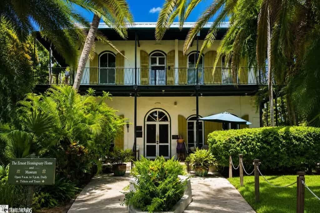 A two-story Hemingway House and Museum with arched windows and tropical plants in front.