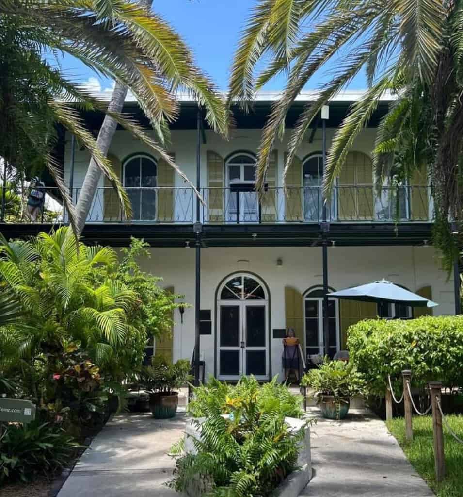 A two-story Hemingway House and Museum with arched windows and tropical plants in front.