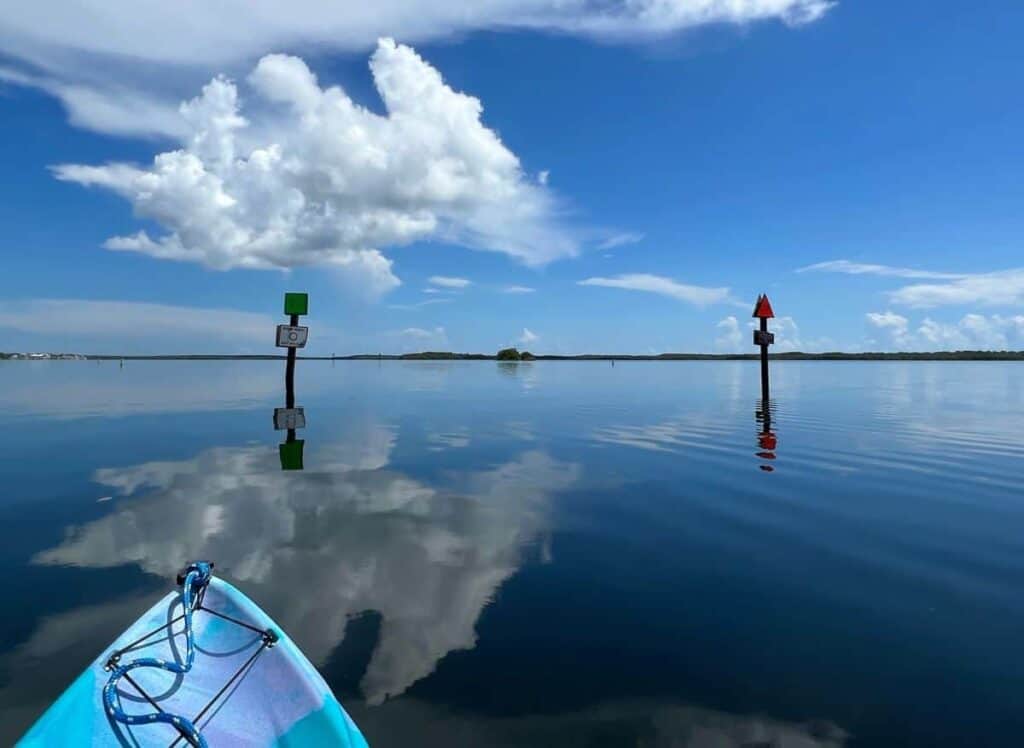 Calm water with sky reflections and two navigation markers, viewed from a blue kayak.