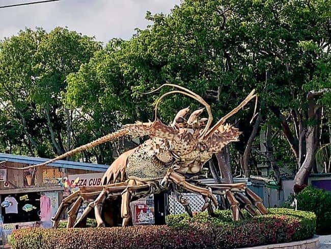 Betsy Large lobster sculpture in an outdoor setting with trees and a small building nearby in the Florida Keys.