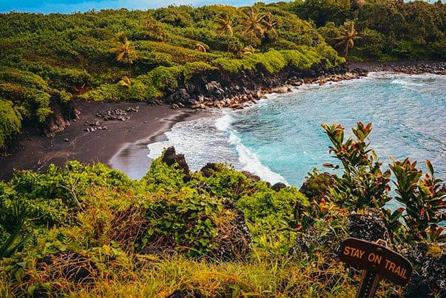 Maui's Waiʻanapanapa State Park: A coastal view with waves crashing over dark rocks, turquoise ocean, and rocky shoreline.
