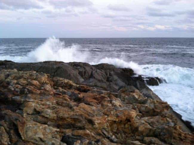 Waves crashing on a rocky shoreline under a cloudy sky.
