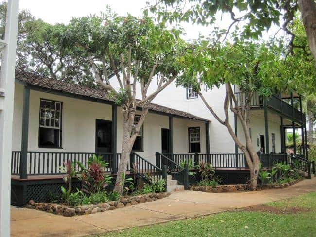 Historic Baldwin House building with green trim, surrounded by trees and a garden.