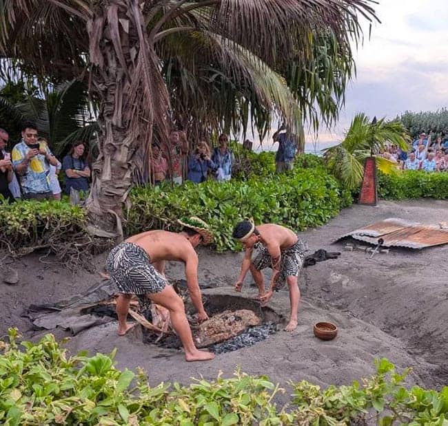 Two people performing a traditional luau cooking ceremony with a crowd watching in Maui.