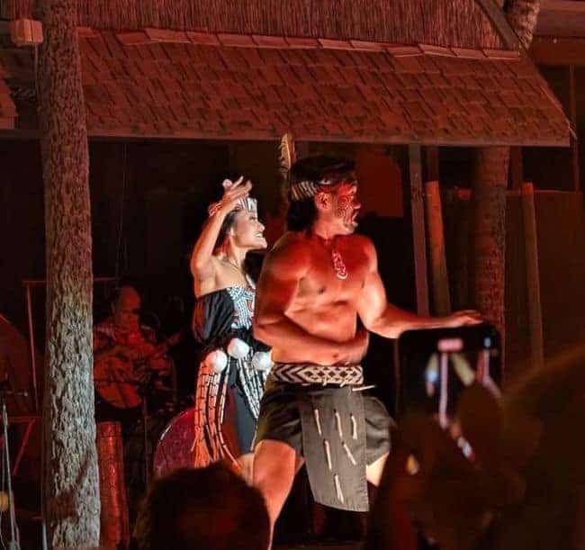 Two dancers performing at a luau, with traditional attire and vibrant stage lighting.