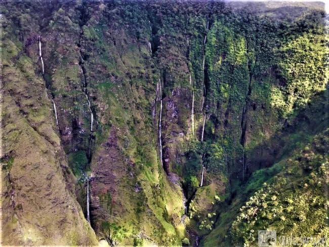 Mana'wai'nui Falls: Aerial view of narrow waterfalls on a lush, green mountainside in vibrant Maui.