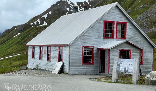 Apartment House Building: Historic gray wooden building with red trim at Independence Mine National Historic Site, Hatchers Pass, surrounded by grassy hills and snow patches.