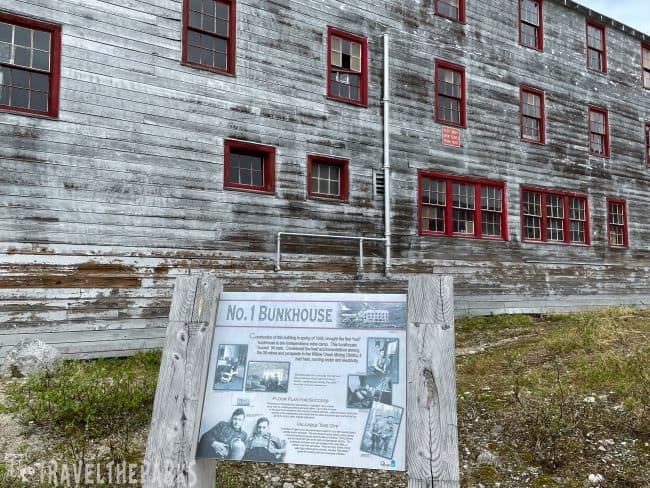 Bunkhouse 1 Building: Old wooden bunkhouse with red-trimmed windows and an informational sign in front.