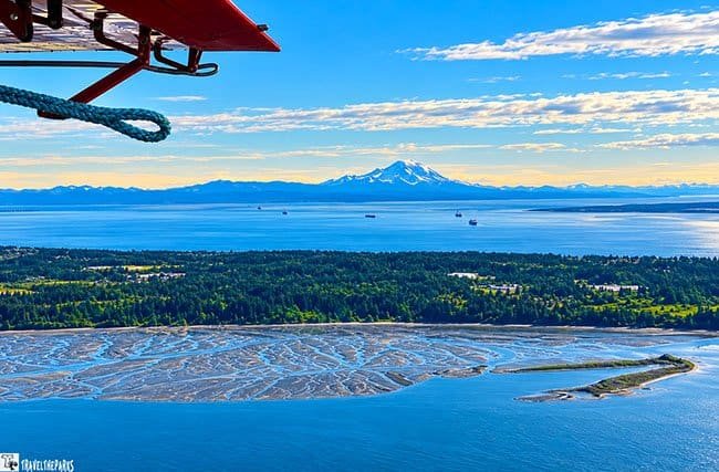 Cooke Inlet: Aerial view of tidal flats, forest, and distant mountains under a cloudy sky, with part of an aircraft visible.